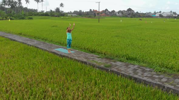 Aerial Slowmotion Shot of a Young Woman Practicing Yoga on a Beautiful Rice Field alt