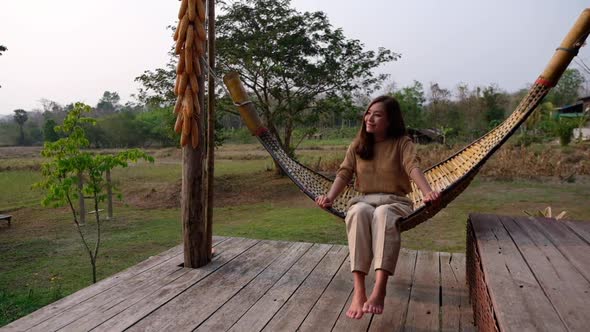 Slow motion of a woman sitting and chilling on wooden hammock