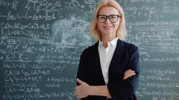 Portrait of Friendly Lady Teacher Standing in Classroom with Arms Crossed Alone alt