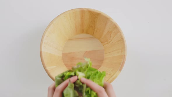 Top view of woman hands showing salad bowl and various green leafy vegetables on the table. alt