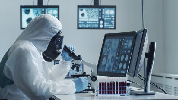 Scientist in protection suit and masks working in research lab using laboratory equipment. alt