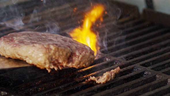Slow motion of beef hamburger on a grill in close up with flames and smoke