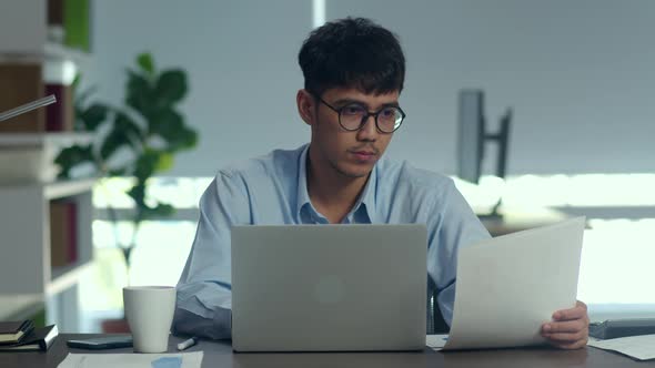Young professional business male using computer looking information paper at office.