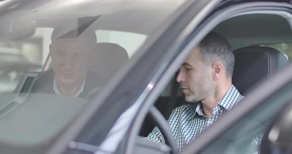 Close-ip Side View of Caucasian Man Sitting in Car Salon and Making Sale Purchase Deal alt