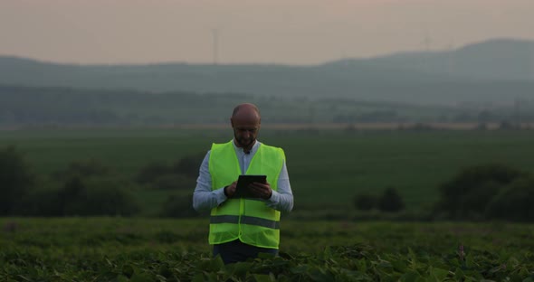 Agricultural Industry. A Male Farmer with a Digital Tablet in a Field at Sunset. Agronomist Uses alt