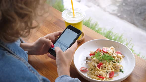 Woman Using Cellphone While Having Dinner At Healthy Vegan Restaurant