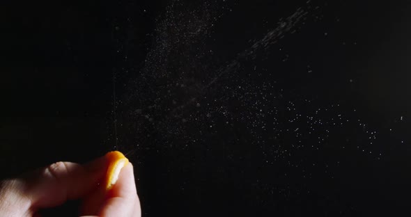 Female Hand Squeezes the Skin of an Orange on a Black Background