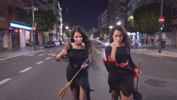 Two Beautiful Colombian Women In Witch Costumes With Broomsticks Walking Fast And Start Running alt