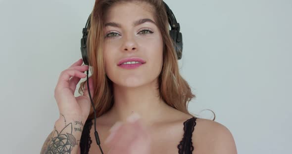 Attractive Woman Puts Headphones Over Ears Light Flirting and Posing at Camera alt