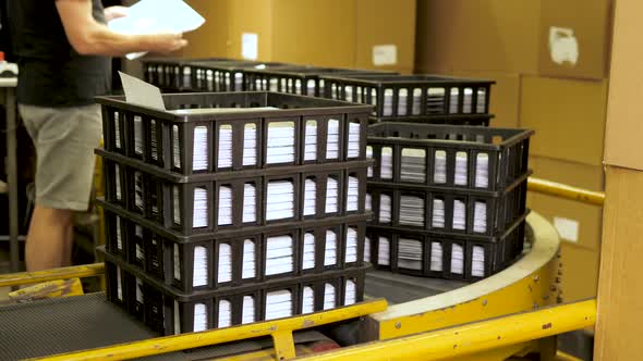 Black crates filled with music vinyl records on a conveyor and checked by worker alt
