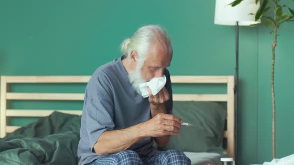 A Sick Elderly Man with Fever Takes Body Temperature with a Thermometer alt