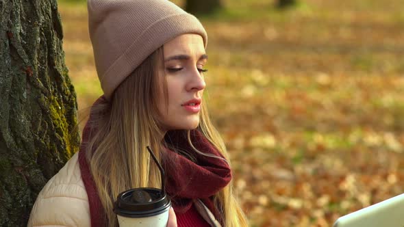 Beautiful Girl, Close-up, Looking at the Laptop Screen. In Autumn Park with Coffee alt