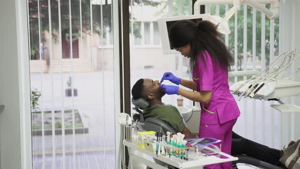 Pretty Young Female African Dentist Examining Her Handsome Male Dark Skinned Patient with alt