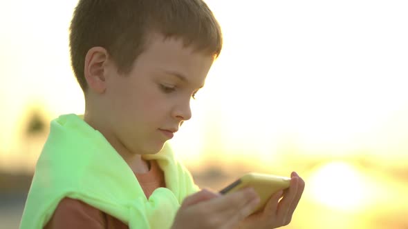 Preschooler Playing Games on the Phone Against the Backdrop of Sunset