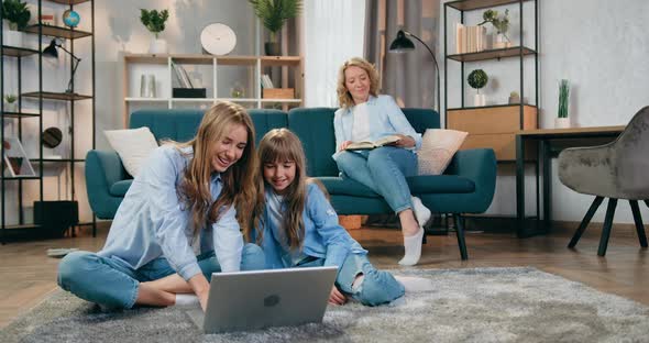 Friendly Two Sisters Sitting on the Floor and Use Laptop and then Waving Hands to Say Hallo alt