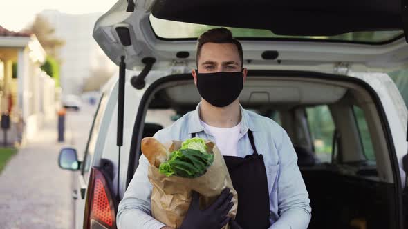 A Movement Shot of a Delivery Man Wearing Protective Face Mask Carrying Groceries Standing Outdoors alt