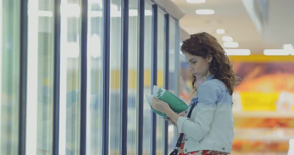 Girl Takes a Package of Frozen Vegetables From the Refrigerator in the Store alt