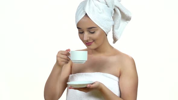 Girl in White Towel on Her Head Holds a Cup and Drinks Coffee or Tea Isolated on White Background alt