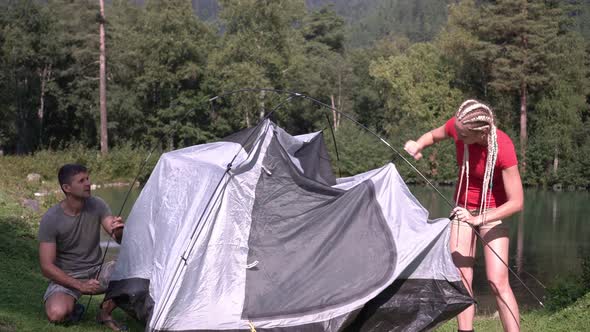 Happy Couple of Hikers on a Hike Put Up a Tent By the Lake in the Forest alt