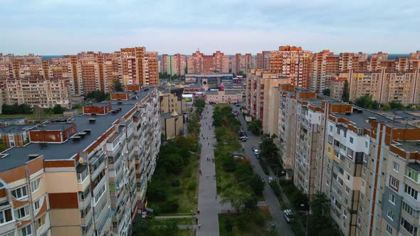 Aerial view over people on the Vyhurivskyi blvd, surrounded by sunlit apartment buildings, in Troies alt