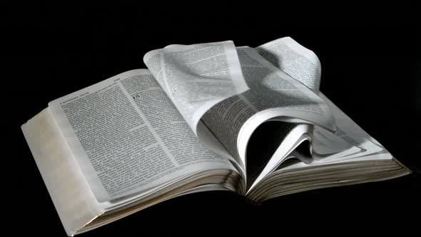 Bible pages turning in the wind on black background alt
