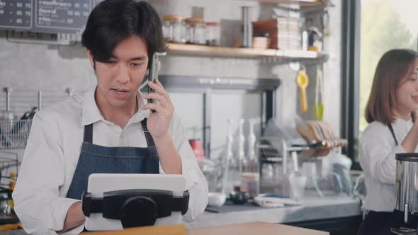 barista man coffee maker receive phone call and record pre order to computer in coffee cafe shop alt