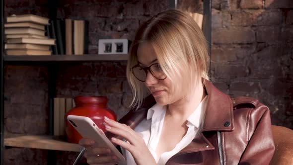 A Young Business Woman Blonde With Glasses Looking Down Using A Smartphone  alt