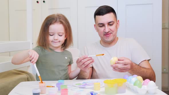 Young Handsome Man with Funny Little Child Paints Bright Colors of Chicken Eggs with a Brush alt