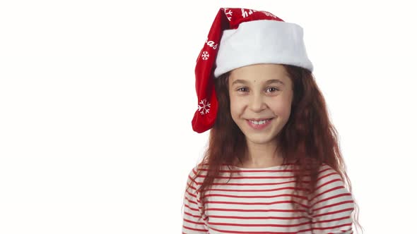 A Girl in a Santa Claus Cap Smiles at the Camera alt