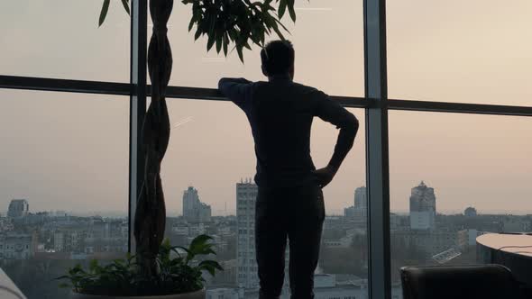 Silhouette Businessman Stands Near Tall Window In Office. Man Stand Near Window On Evening City. alt