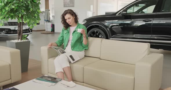 Young Beautiful Girl Flips Through Magazine and Selects New Car at Car Dealership. Buyer Selects Car alt