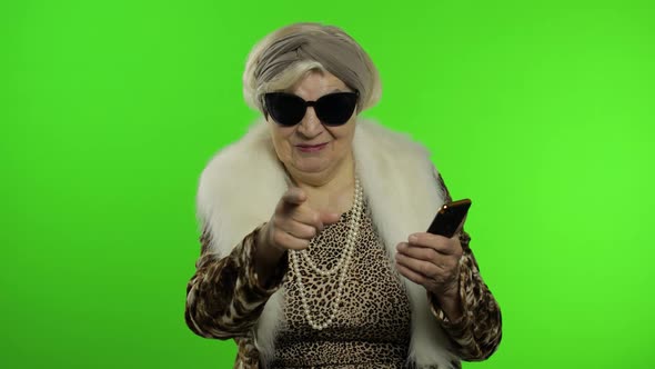 Caucasian Grandmother Woman Using Smartphone, Pointing at Camera with Hand alt