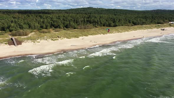 AERIAL: Surfer with Kite Visible in the Forest and Sandy Beach Background alt