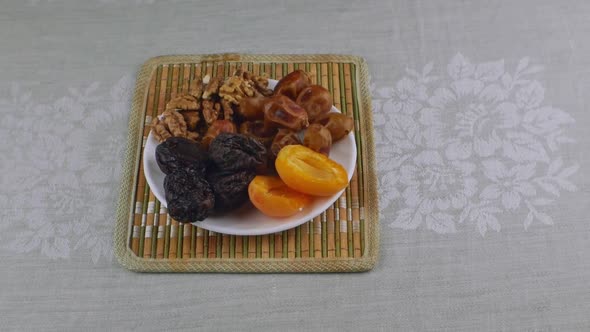 Apricots Prunes Dates Walnuts on a White Saucer Standing on a Bamboo Napkin alt