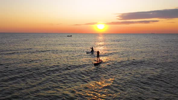 Two stand up paddlers enjoy tropical island sunset in the ocean. Travel concept alt