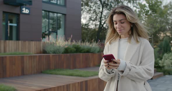 Female Pretty Person Using Smartphone While Walking at City Street. Beautiful Young Woman Typing alt