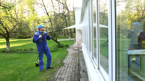Man Washing Conservatory Window With Water Jet Reflecting On Glass