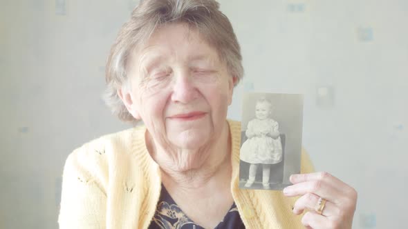 Senior Woman Holding up an Old Photograph of Herself