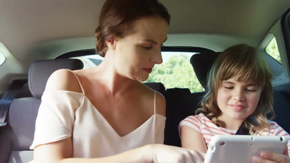 Mother and daughter using digital tablet in the back seat of car alt