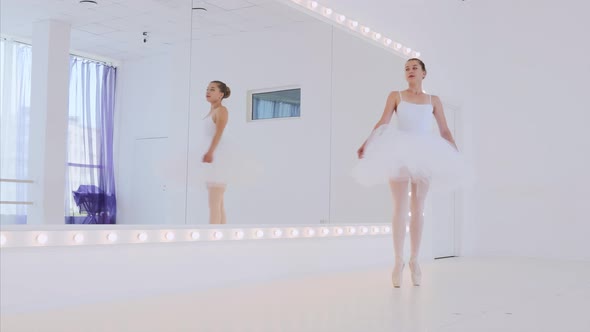 Ballerina in White Tutu is Practicing Dance Elements in Front of the Mirror