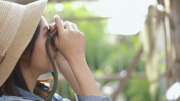 Portrait of Asian woman wearing retro fedora hat use film camera taking a photo at a small street. alt
