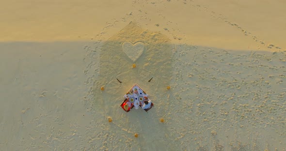 Aerial drone view of a man and woman eating dinner and dining on a tropical island beach alt