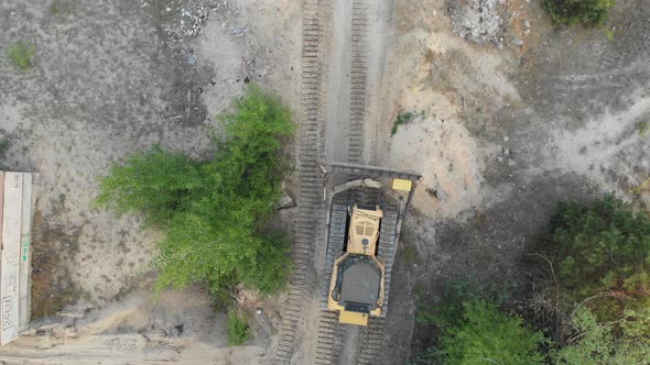 Top Aerial View on Tracked Bulldozer Rides on Sandy Road at Construction Site alt