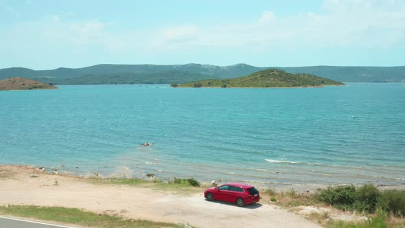 Auto on Steep Beach Against Hilly Green Islands in Azure Sea alt