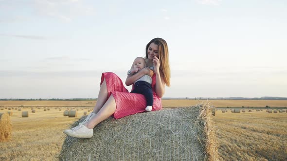 Lovely Mother Relaxing with Her Baby Son on a Haycock Caressing Him and Smiling alt