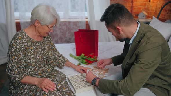Relatives Grandmother and Her Oldest Grandson Playing Vocabulary Puzzles Together in Her Bedroom alt