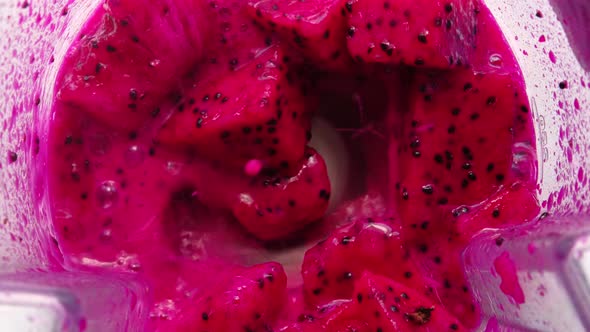 Top view of red dragon fruit mixing into blender seen from inside.