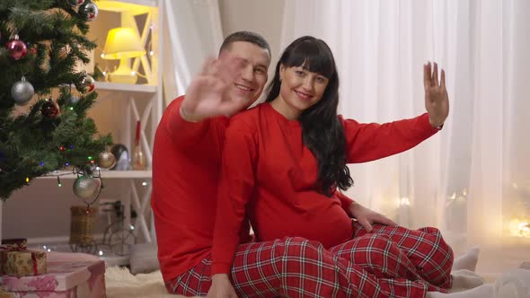 Happy Smiling Pregnant Woman and Man in Similar Red Pajamas Looking at Camera Waving in Slow Motion alt