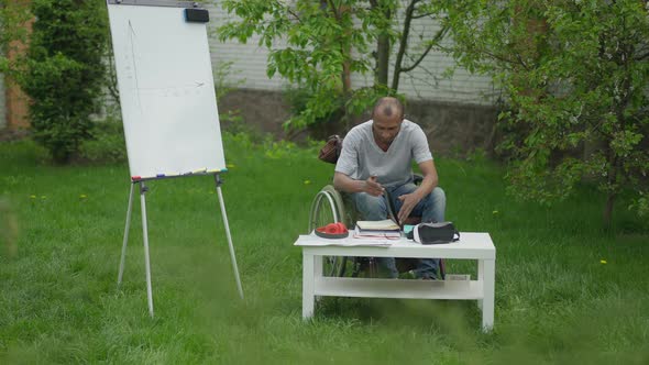 Wide Shot of Confident African American Man in Wheelchair Turning Pages of Worksheet Sitting in alt