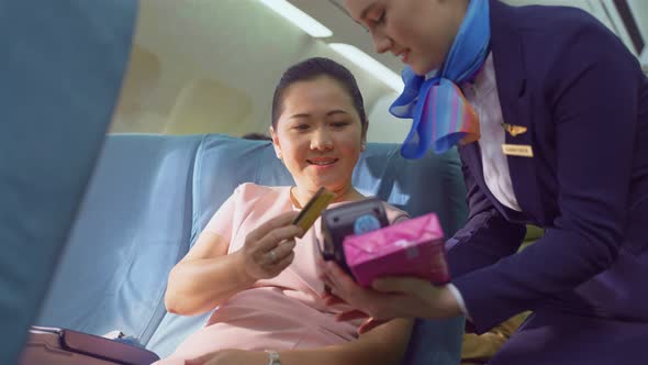 Onboard product purchasing, Asian woman sit in airplane use credit card buy gift from air hostess. alt